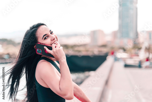 Close up portrait of young woman who's talking by phone and smiling in the city street. In a distance connecting concept © Nina Nagovitsina