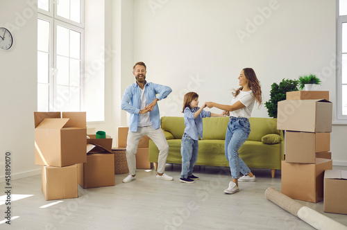 Happy family having fun in house of their dream. Cheerful mom, dad and kid playing and dancing in room with sofa and unpacked boxes in new home. Real estate, mortgage, buying and moving house concept