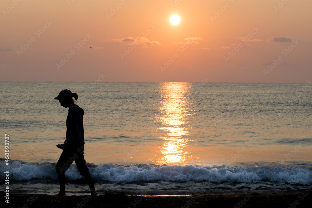 A girl, a teenager walks alone on the beach at sunrise. Loneliness, future plans - concept. Silhouette. 