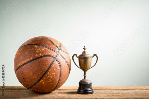 still life photography : vintage trophy with old basketball on wooden table against space of wall