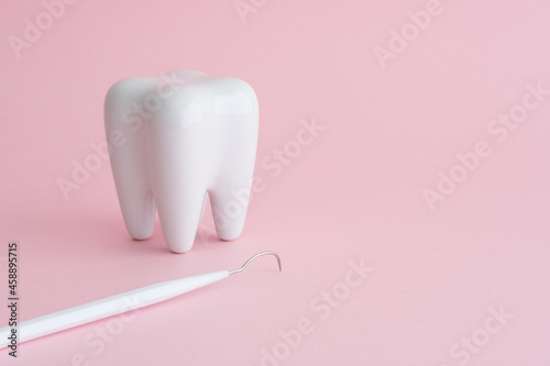Fototapeta Naklejka Na Ścianę i Meble -  White healthy tooth model and dental pick explorer probe on pink background with copy space. Dental care and healthcare concept.