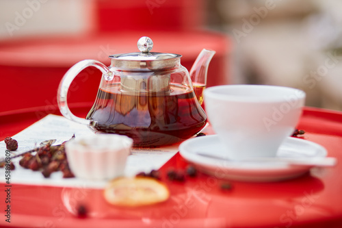 Hot tea in glass teapot and cup, on red background