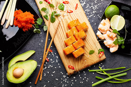 Set of various sushi rolls with soy sauce, srimps and chopsticks over dark background photo