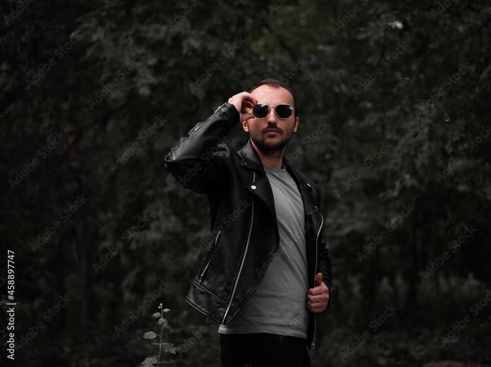 А man with a beard straightens his sunglasses on the background of the forest А man with a beard straightens his sunglasses on the background of the forest