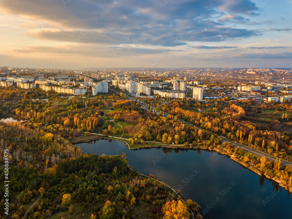 Fototapeta premium Aerial view of a lake in a park with autumn trees. Kishinev, Moldova. Epic aerial flight over water. Colorful autumn trees in the daytime.