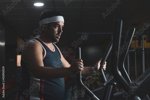 a funny fat boy doing sports inside a gym.
overcoming concept.
willpower. photo