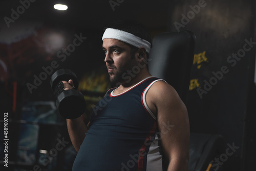 a funny fat boy doing sports inside a gym. overcoming concept. willpower. ©  Yistocking