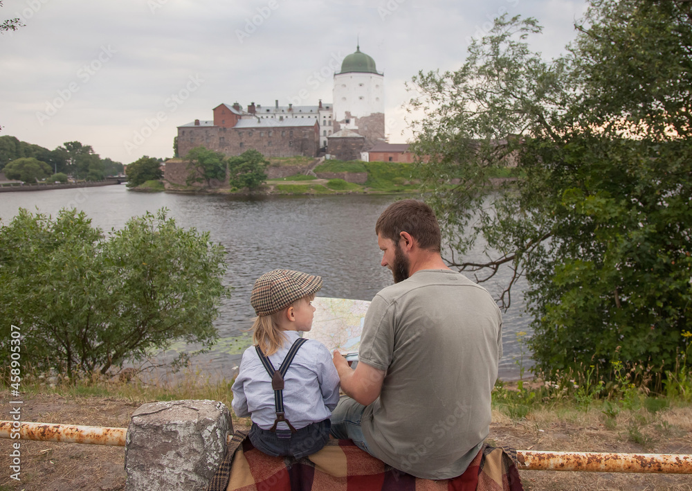 Naklejka premium a father and son in vintage clothes are sitting and looking at an ancient city. They have a map and they are discussing the way. View from the back