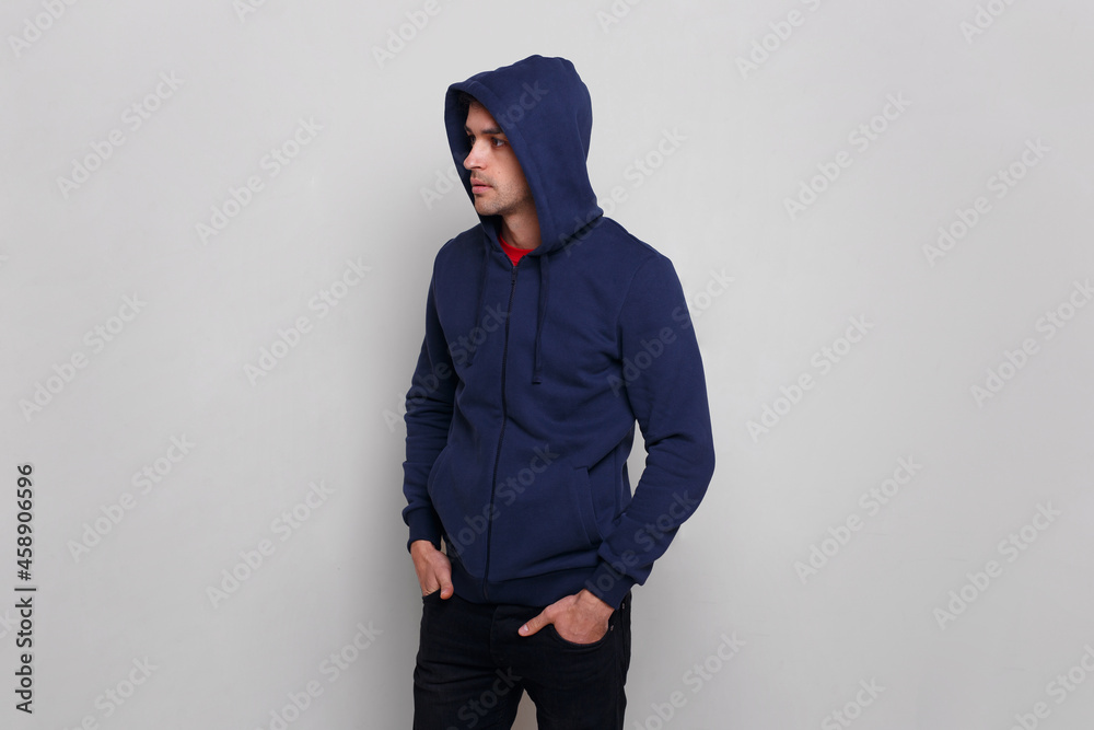 Profile of a young man in dark blue jumper and jeans, with a hood on his head, isolated grey background.
