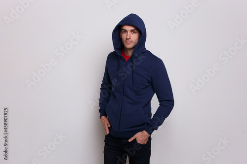 Frontal of a young man in dark blue jumper and jeans, with a hood on his head, isolated grey background.