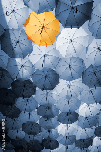 Background of blue umbrellas with one standing out in yellow. The different one from the crowd. photo