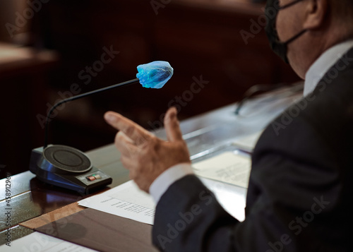 Crop businessman in mask talking in mic during conference