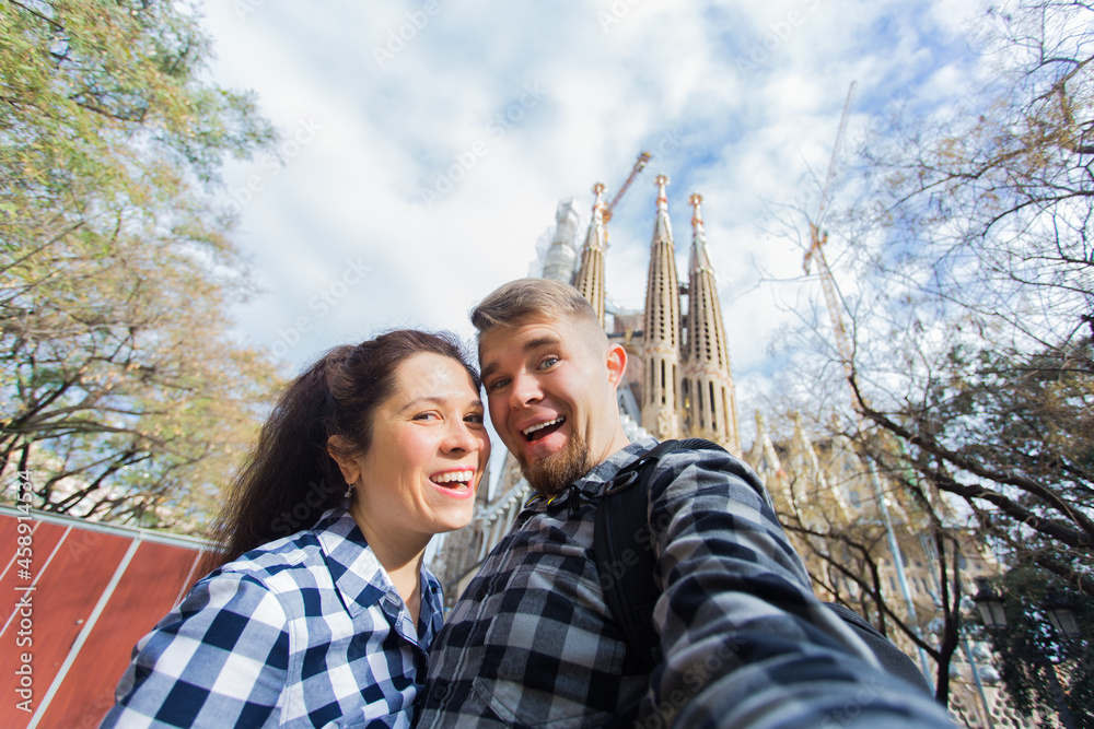 Happy couple making selfie photo in front of the famous Sagrada Familia catholic cathedral. Travel in Barcelona