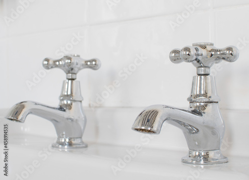 Vintage chrome taps on sink  white tiled background in bathroom  close up