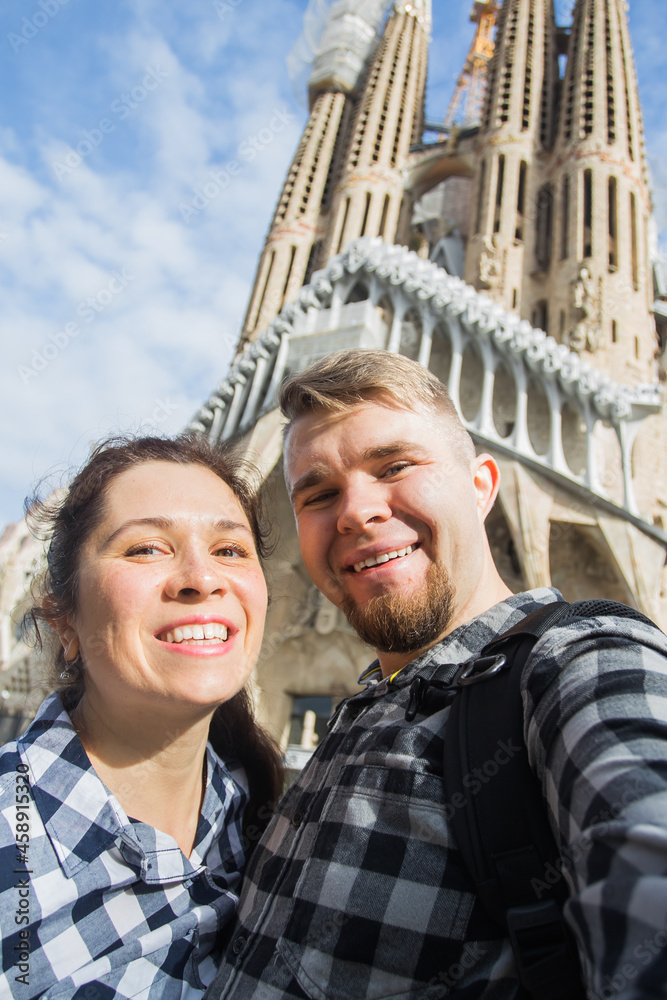 Happy tourists photographing in front of the famous Sagrada Familia roman catholic church in Barcelona, architect Antoni Gaudi