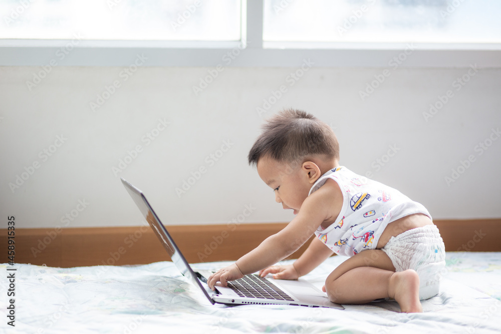 Adorable infant baby boy playing on laptop computer look so busy Adorable infant baby boy playing on laptop computer look so busy