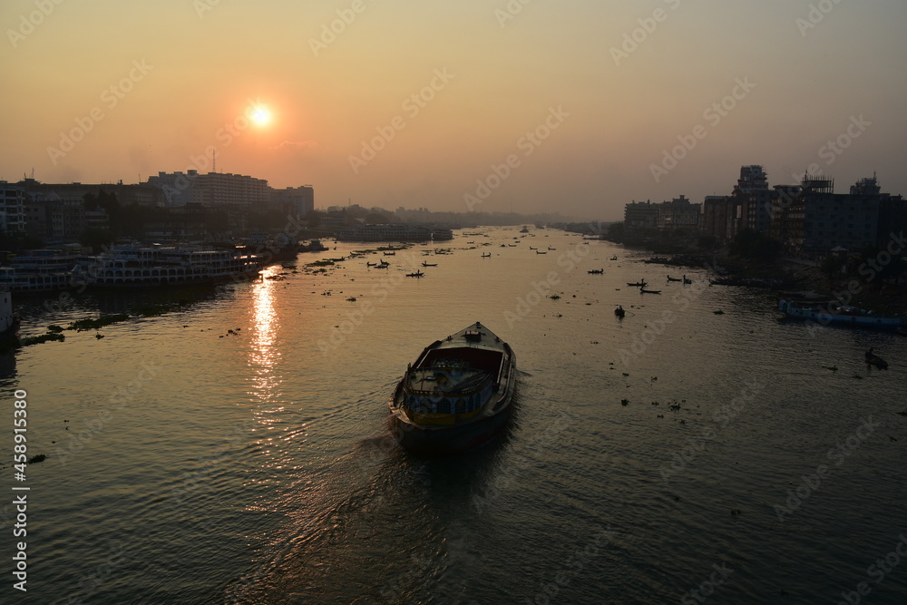 Naklejka premium バングラデシュの首都。 早朝のダッカ。 美しい朝日と川を進むタンカー。