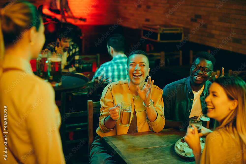 Obraz premium Happy friends having fun while drinking beer and talking to waitress in a bar.