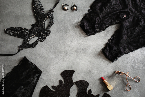 Flat lay composition with black sexy lace face mask and lingerie for Halloween party on grey background, top view from above