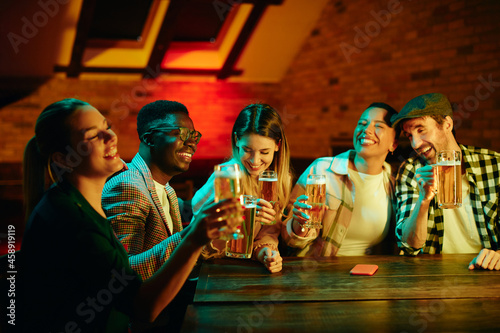 Group of young happy people having fun while drinking beer in a bar at night.
