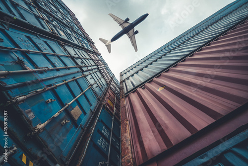 Freight airplane flying above overseas shipping container . Logistics supply chain management and international goods export concept .