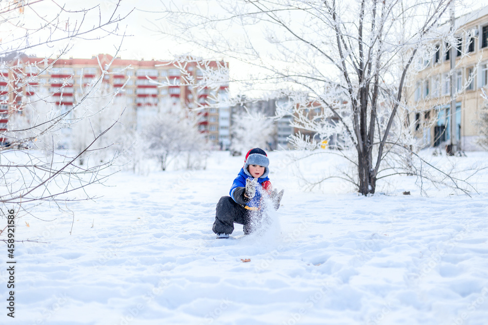 Little boy having fun playing with fresh snow. Snow fight. Kid dressed in a warm clothes, hat, hand gloves.. Active outdoors leisure for child on nature in snowy winter day.