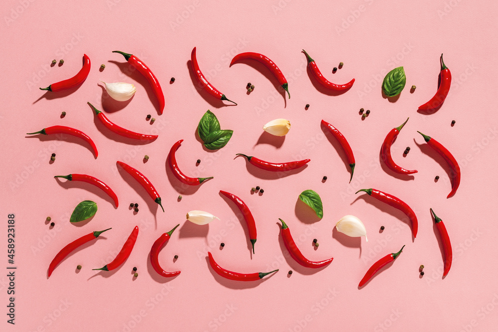 Raw red hot chili peppers, few garlic cloves and fresh green basil leaves, black pepper grains cast harsh shadows on a pastel coral pink background. Spice creative composition with hard light. Raw red hot chili peppers, few garlic cloves and fresh green basil leaves, black pepper grains cast harsh shadows on a pastel coral pink background. Spice creative composition with hard light.