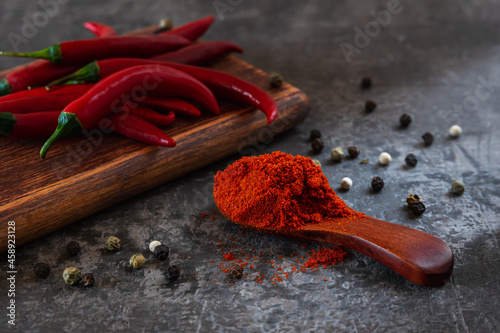 Close-up of сhili powder in a wooden spoon near red hot chilli peppers on a chopping board. ground chili pepper and whole raw chiles as spicy ingredient for pungent meat dishes. Low key image.