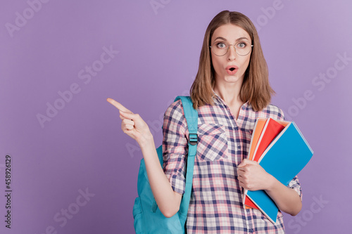Portrait of young girl student holding notebook point finger empty space choose amazed isolated on violet color background