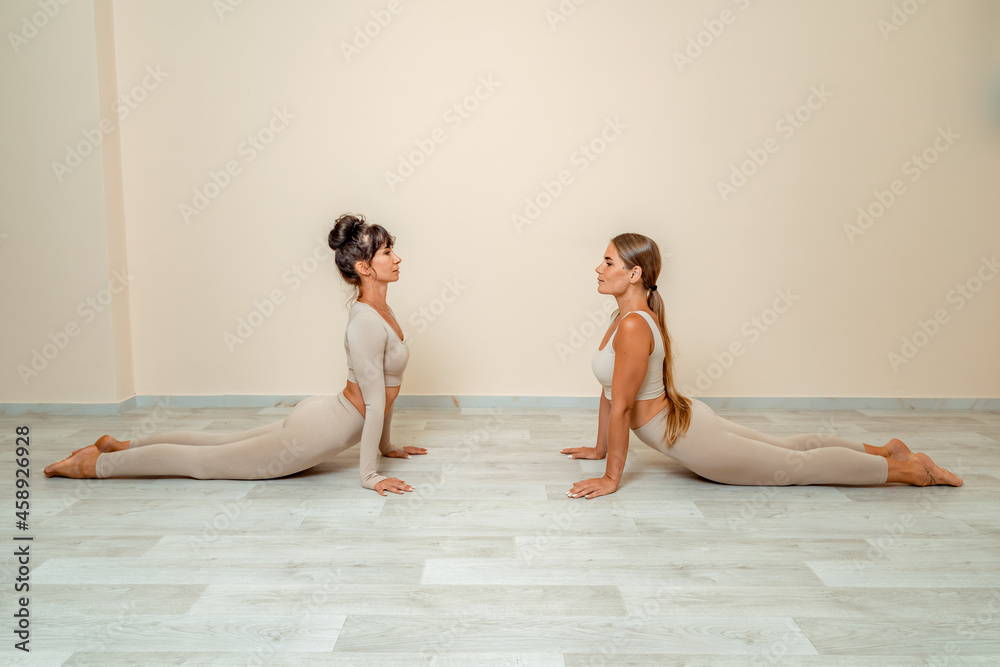 Fitness, pilates stretching exercises, a group of two attractive smiling mature women in beige sports clothes, train in a sports club. Fitness, pilates stretching exercises, a group of two attractive smiling mature women in beige sports clothes, train in a sports club.