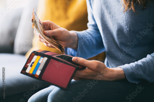 Woman putting cash money in her wallet at home