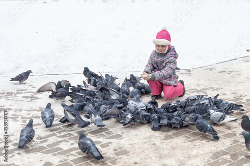 A girl in winter clothes sat down and feeds pigeons with crumbs. saving the pitz from starvation in winter photo