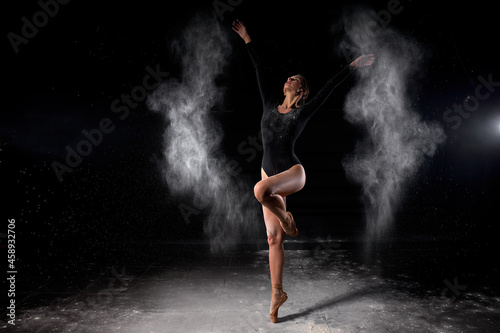 Dancer posing dancing gracefully in studio with cloud of dust, flour. Dancer in black bathing suit is moving, in action, having good choreographic training. ballet, dance, performance, art © alfa27