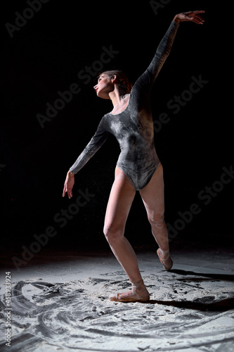 Fototapeta Naklejka Na Ścianę i Meble -  Dancing in flour concept. athlete woman dancer in flour. Female making dance element on black background in studio, isolated. black bodysuit is in powder. graceful ballet dancer portrait