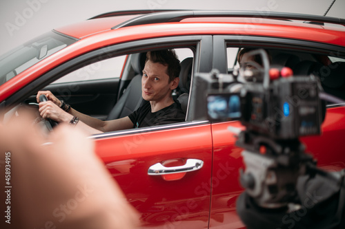 Professional male actor works in the frame on the set. Shooting with a car on a large white cyclorama.