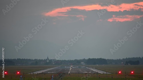 Small ultralight airplane landing at Ljubljana Airport, Slovenia. Telephoto perspective of ultra light aircraft arrival. Colorful summer sunset. Static shot, real time photo
