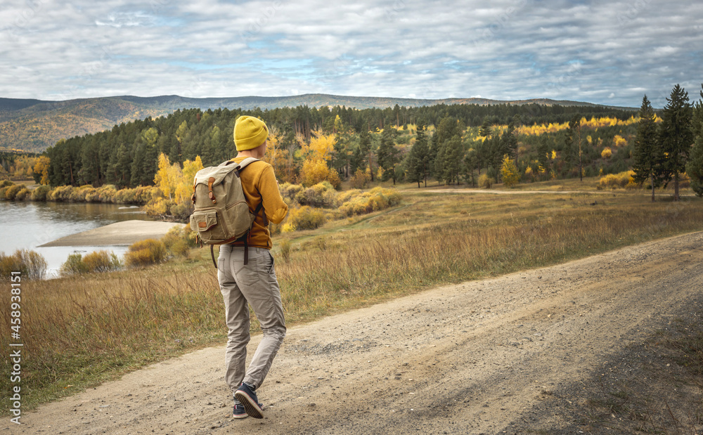 Traveler with a backpack is walking on an empty road along forest. Concept of freedom, travel, hiking and autumn mood Traveler with a backpack is walking on an empty road along forest. Concept of freedom, travel, hiking and autumn mood