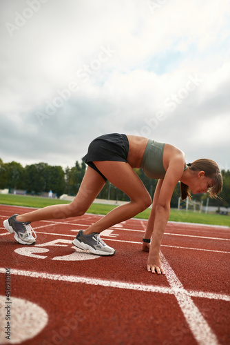 Side view of young female runner start running on track field in the daytime