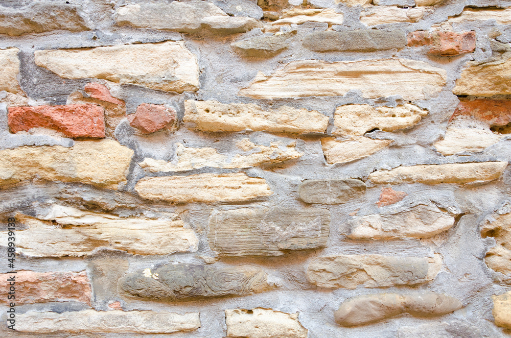A wall of stones and bricks of various shapes and sizes in a large amount of cement mortar A wall of stones and bricks of various shapes and sizes in a large amount of cement mortar