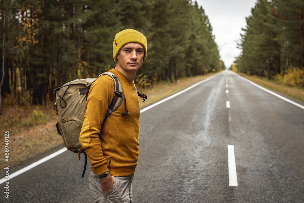 Traveler with a backpack is walking on an empty road along forest. Concept of freedom, travel, hiking and autumn mood Traveler with a backpack is walking on an empty road along forest. Concept of freedom, travel, hiking and autumn mood