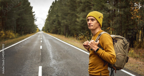 Traveler with a backpack is walking on an empty road along forest. Concept of freedom, travel, hiking and autumn mood