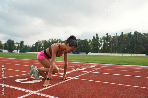 Professional young female runner in sportswear getting ready to start running on track field at stadium