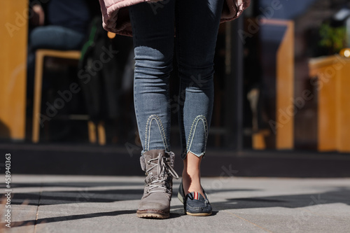 Girl wearing different shoes on her feet. Boots and sandals. Outdoor shot on a street..