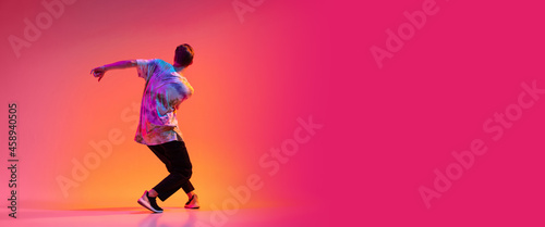Back view of young stylish man dancing hip-hop isolated over colorful gradient background in neon light. Flyer photo