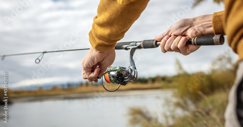 Male hands of a fisherman are holding a spinning closeup. Concept of fishing in the autumn forest