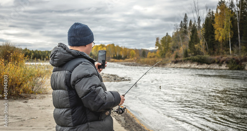 Man is standing on the river bank in the autumn forest with a fishing rod in his hands and catching fish