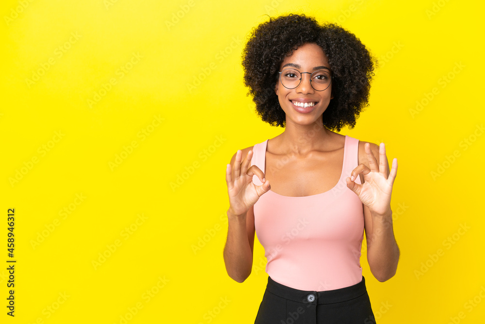 Young African American woman isolated on yellow background showing ok sign with two hands