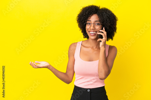 Young African American woman isolated on yellow background keeping a conversation with the mobile phone with someone