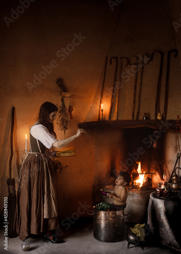 Witch with magic book conjuring over cauldron with child photo