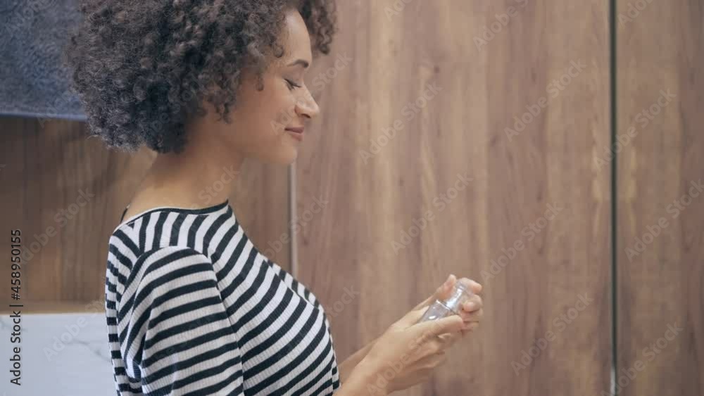 Pretty curly-haired woman spraying perfume, smiling in bathroom mirror, glamour Pretty curly-haired woman spraying perfume, smiling in bathroom mirror, glamour